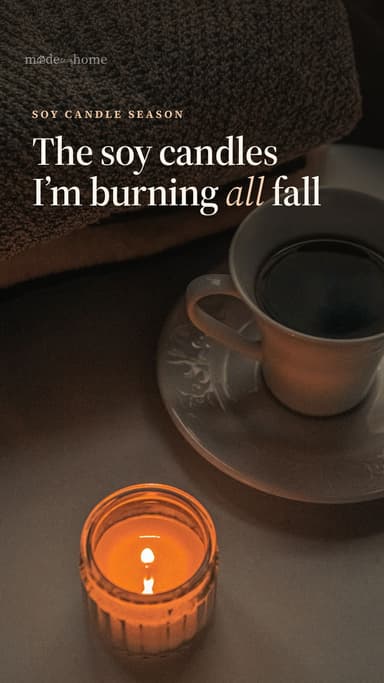 Lit soy candle beside a cup of coffee and a knit throw