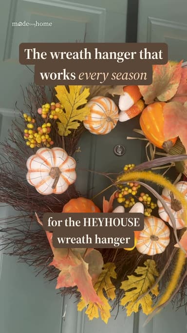 Fall wreath with pumpkins and leaves hanging on a sage green front door
